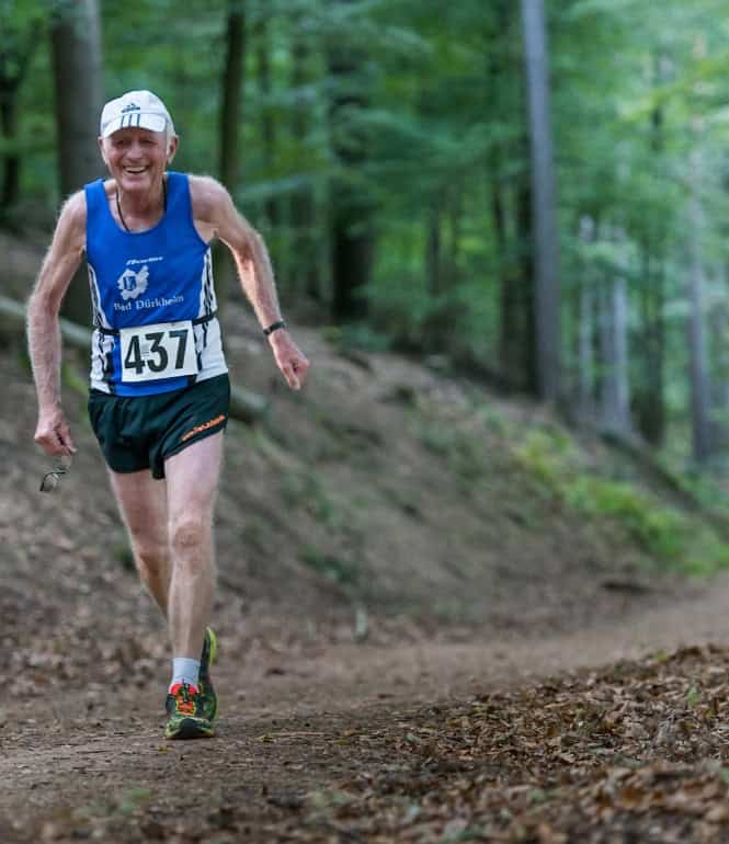 Älterer Läufer mit Startnummer 437 und blauem Shirt läuft auf einem Waldweg