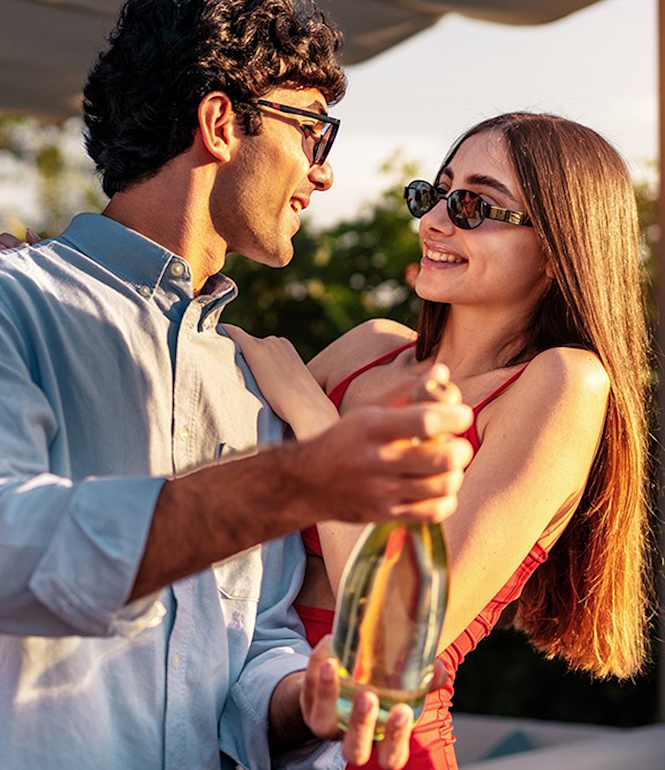 Paar hält eine Flasche und lacht gemeinsam bei Sonnenuntergang