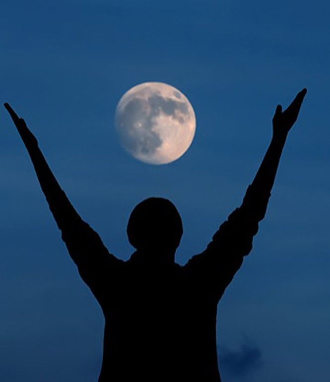 Silhouette einer Person mit erhobenen Armen vor Vollmond