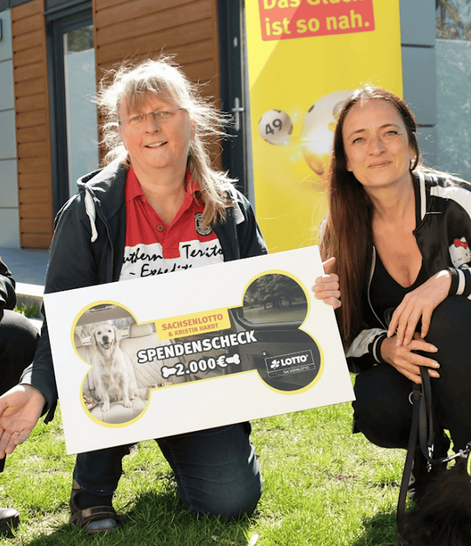 Magdalena Bartmann von Sachsenlotto übergibt gemeinsam mit Kristin Hardt einen 2.000-Euro-Spendenscheck aus der Lucky Dog Aktion an Sabine Kaden vom Tierheim Gröbern. Bartmann hält Lucky Dog Rubbellose in der Hand.