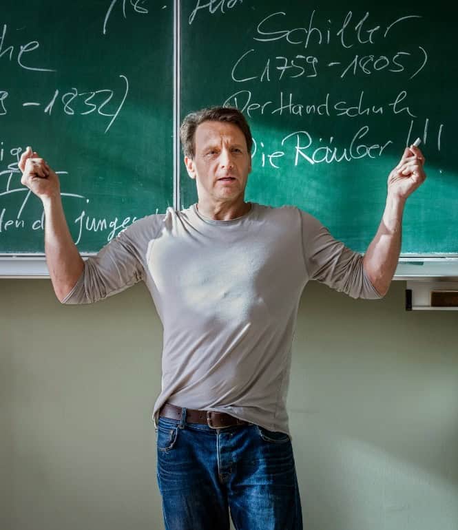 Schauspieler Hendrik Duryn als Lehrer Stefan Vollmer steht vor einer Kreidetafel in einem Klassenzimmer.
