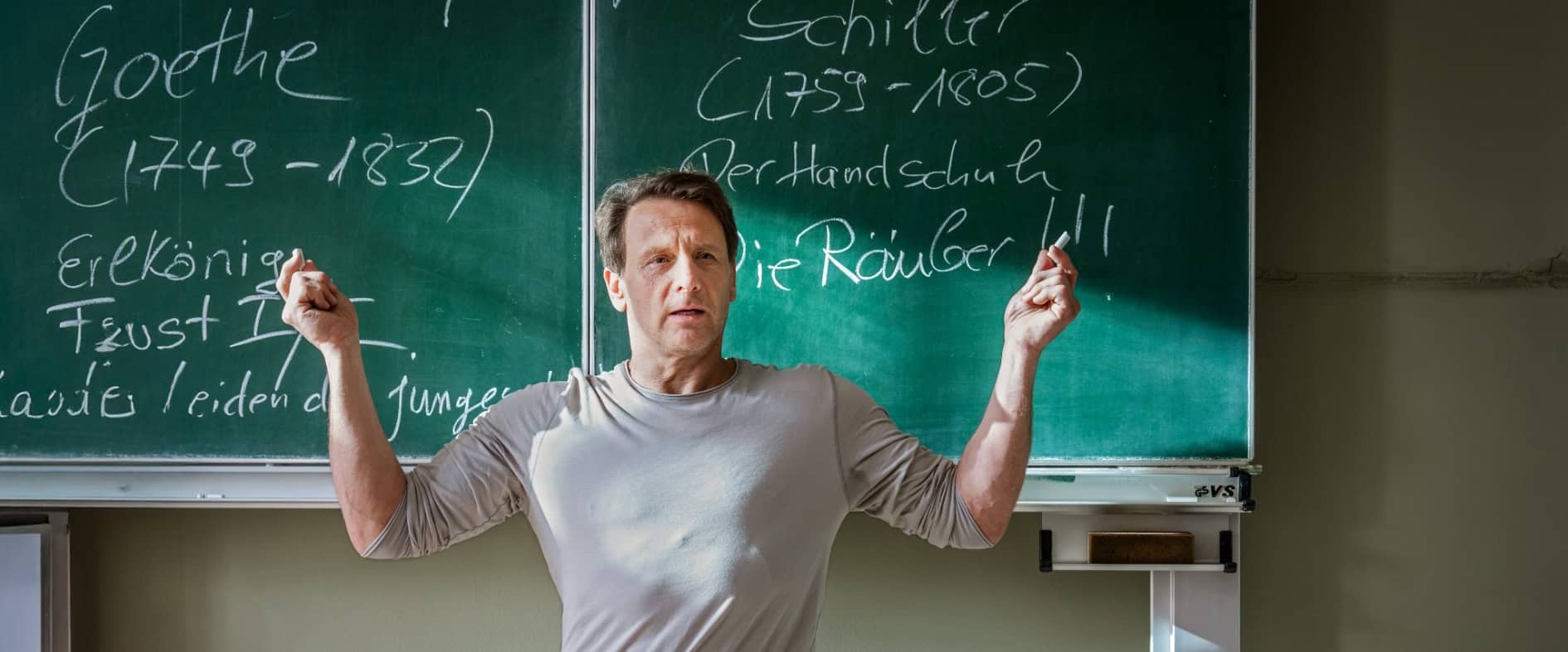 Schauspieler Hendrik Duryn als Lehrer Stefan Vollmer steht vor einer Kreidetafel in einem Klassenzimmer.
