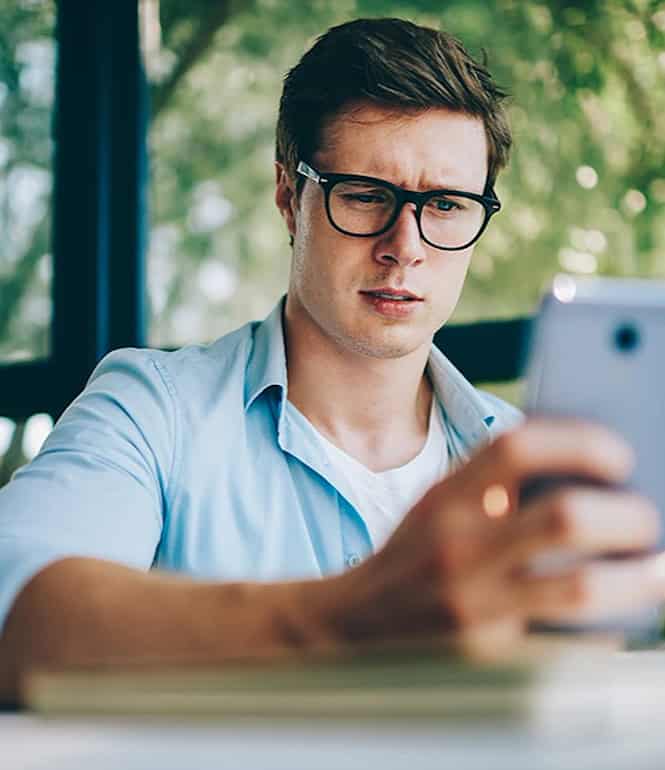 Mann mit Brille schaut skeptisch auf sein Smartphone.