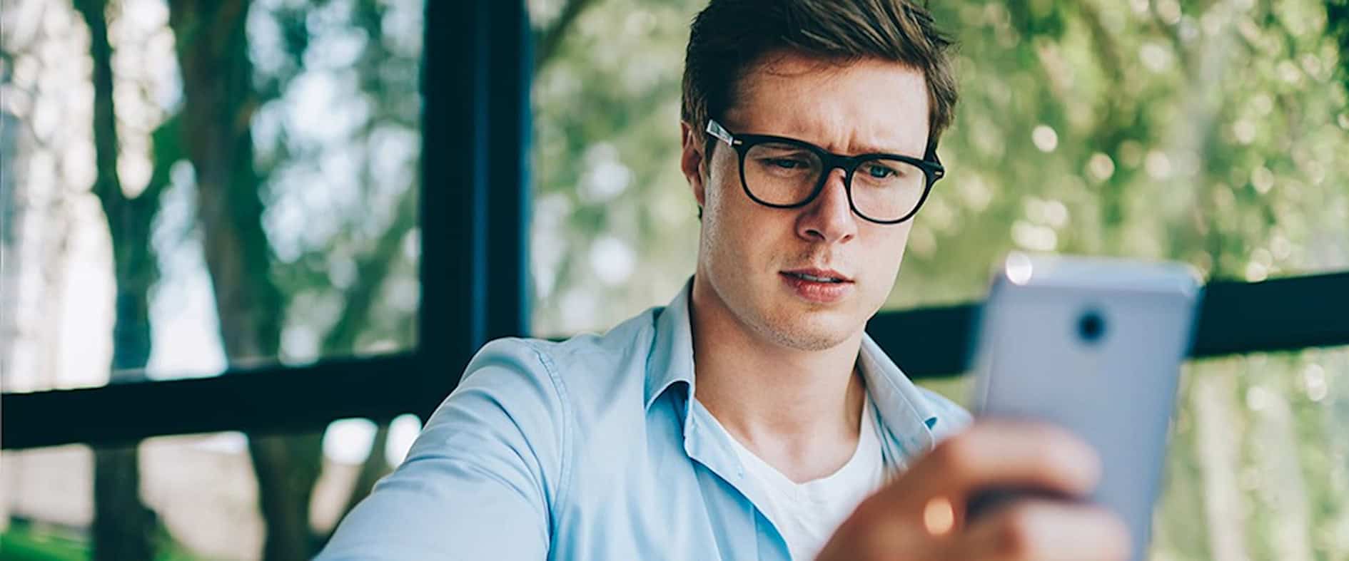 Mann mit Brille schaut skeptisch auf sein Smartphone.
