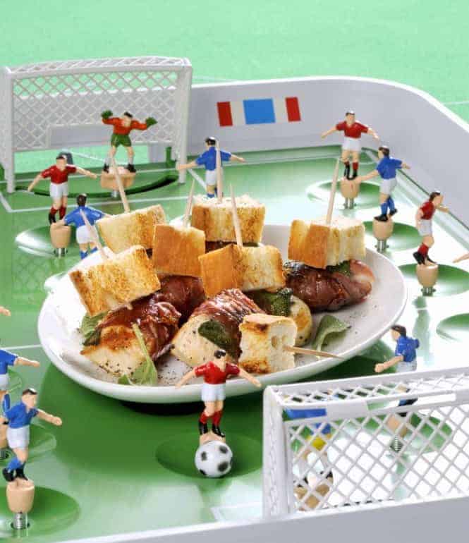 Hähnchennuggets mit Speck und Salbei auf einem Teller, arrangiert wie ein Fußballspiel mit Miniatur-Fußballspielern und Toren.