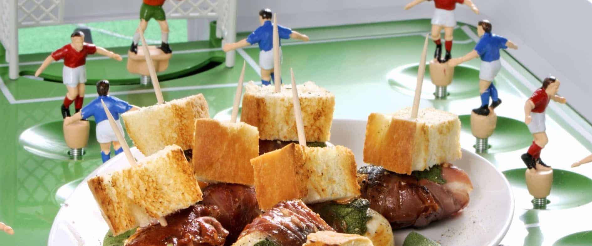 Hähnchennuggets mit Speck und Salbei auf einem Teller, arrangiert wie ein Fußballspiel mit Miniatur-Fußballspielern und Toren.