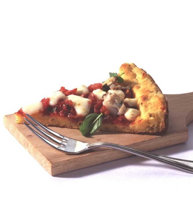 Stück Kartoffelkuchen mit Venusmuscheln, Tomatensauce und Mozzarella auf einem Holzbrett, garniert mit Basilikum.