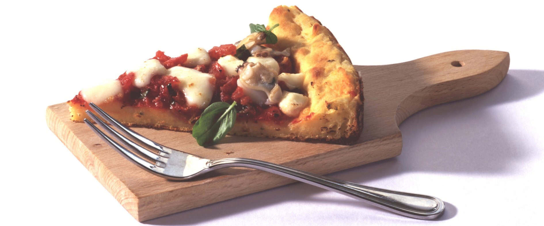 Stück Kartoffelkuchen mit Venusmuscheln, Tomatensauce und Mozzarella auf einem Holzbrett, garniert mit Basilikum.