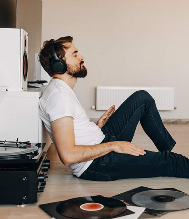 Mann hört entspannt Vinyl-Platten auf einem Plattenspieler – Symbol für analogen Luxus.