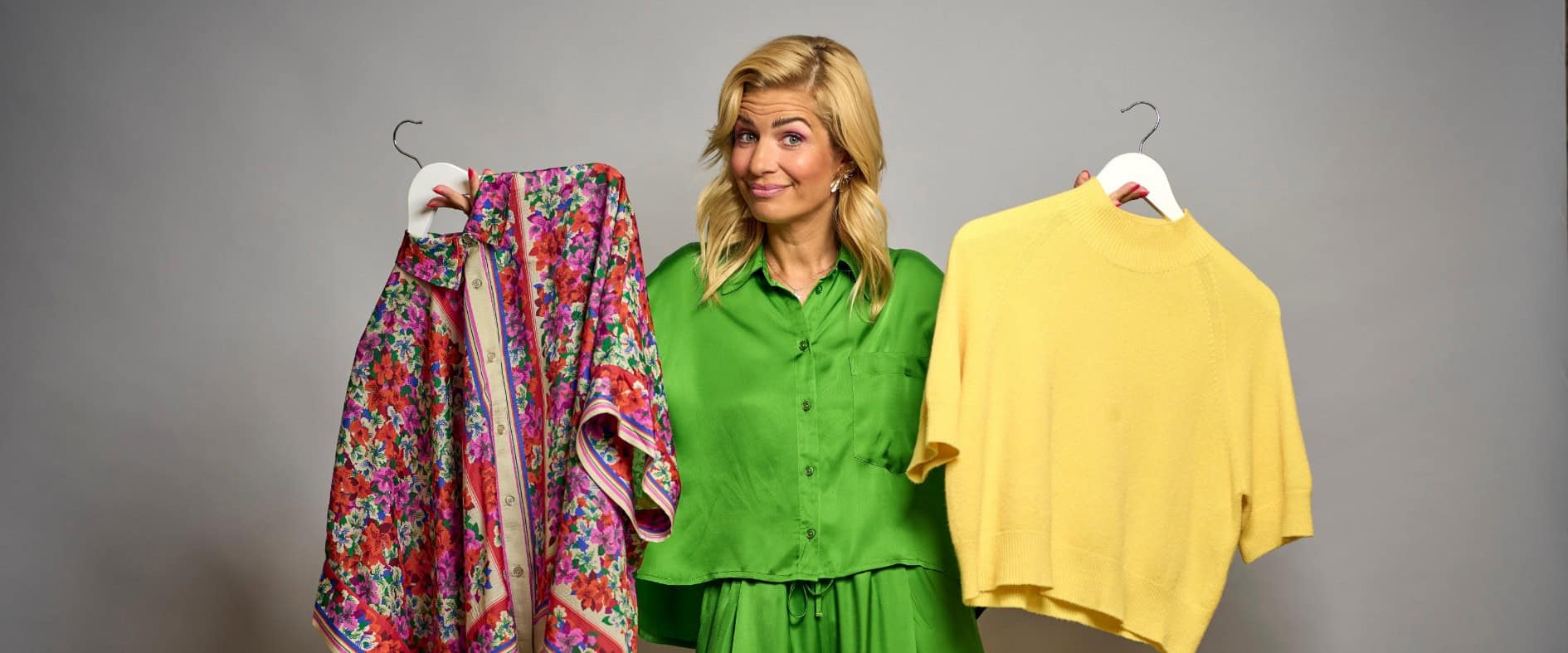 Susan Sideropoulos hält ein buntes Blumenmuster-Shirt und einen gelben Pullover vor sich.