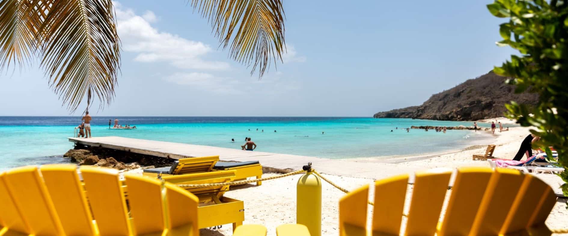 Gelbe Liegestühle an einem Traumstrand von WM-Teilnehmerland Curaçao mit türkisblauem Meer und Palmen