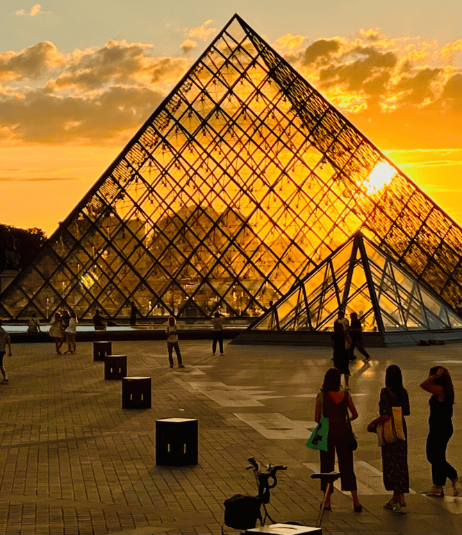 Glaspyramide des Louvre in Paris bei Sonnenuntergang mit Besuchern auf dem Vorplatz des Museums.
