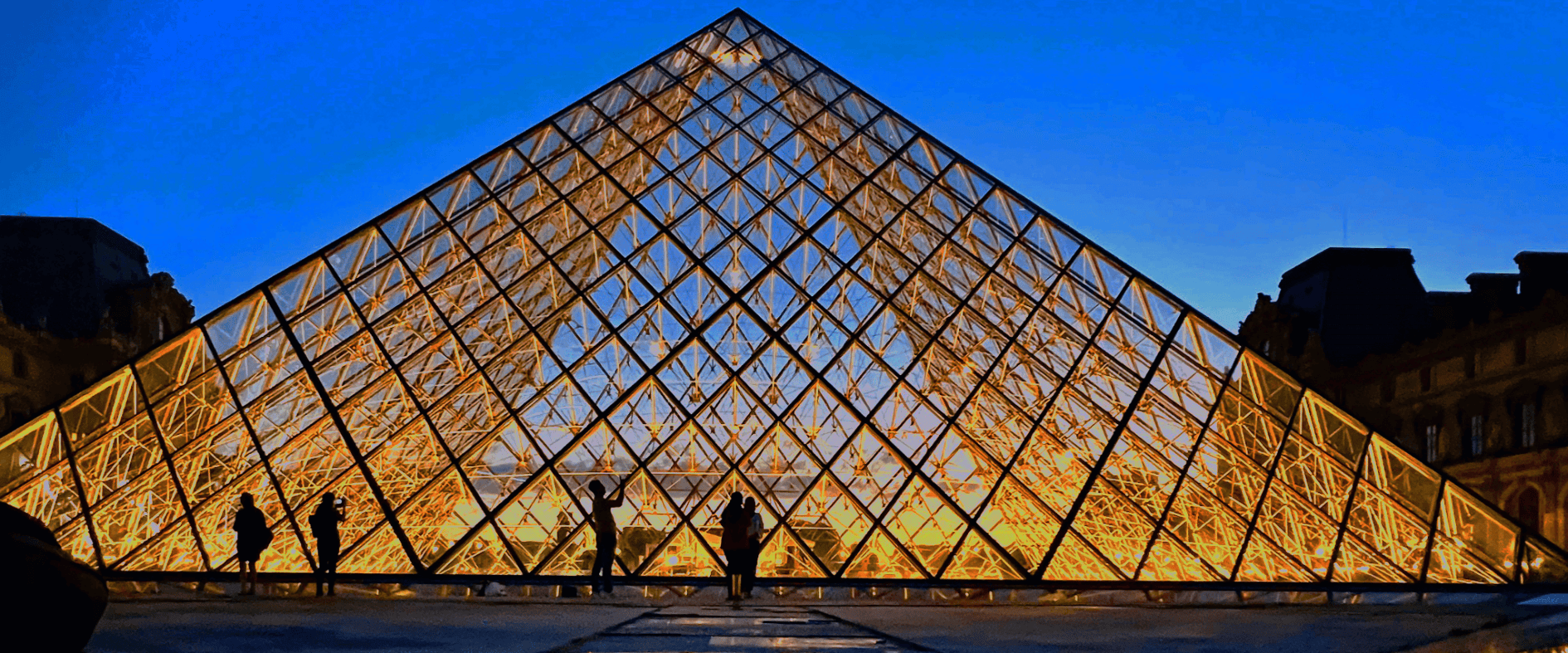 Glaspyramide des Louvre in Paris bei Sonnenuntergang mit Besuchern auf dem Vorplatz des Museums.