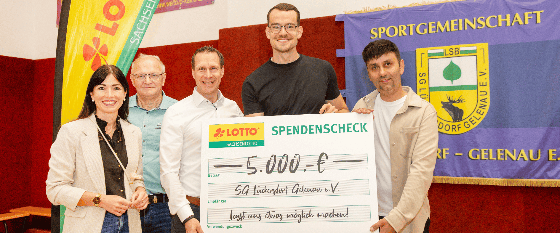 Fünf Personen stehen nebeneinander und präsentieren einen symbolischen Spendenscheck von Sachsenlotto über 5.000 Euro für die SG Lückersdorf-Gelenau e. V.; im Hintergrund sind ein Lotto-Banner und ein Vereinsbanner zu sehen.