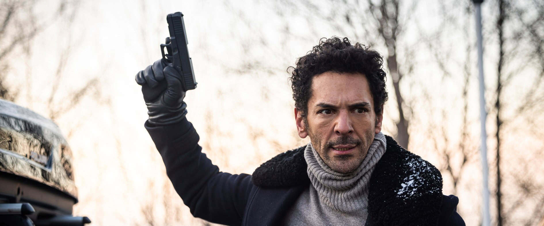 Schauspieler Tomer Sisley als Largo Winch mit gezückter Waffe in einer spannungsgeladenen Szene.