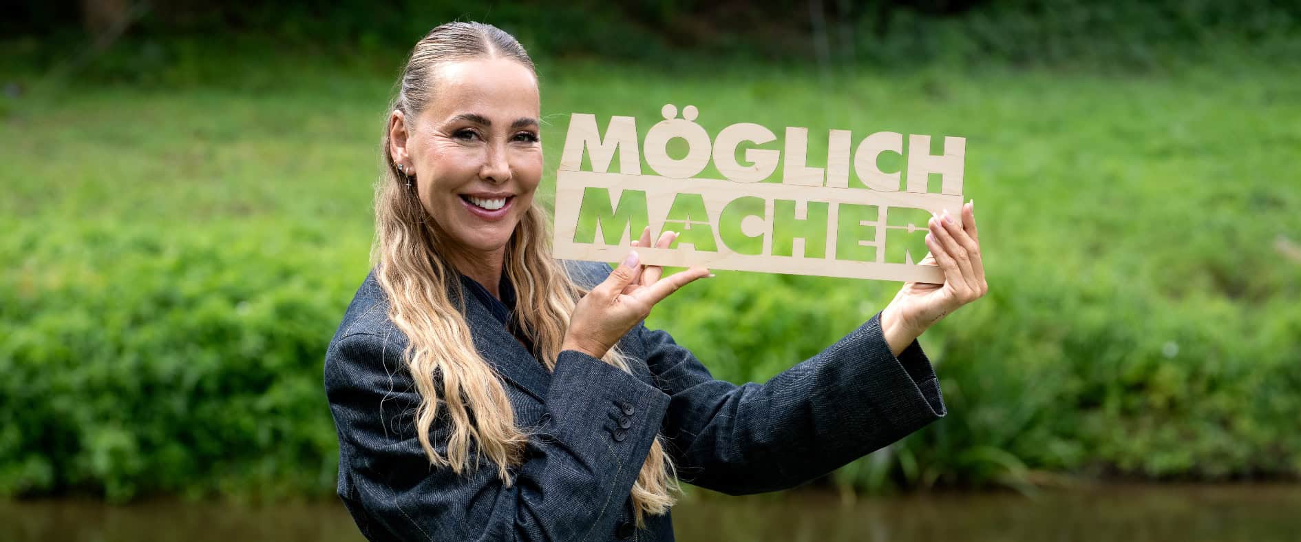 Sylvia Walker präsentiert den Sachsenlotto-Möglichmacher mit Holzschild als Symbol für Engagement, Unterstützung und die vielfältige Förderkampagne in Sachsen