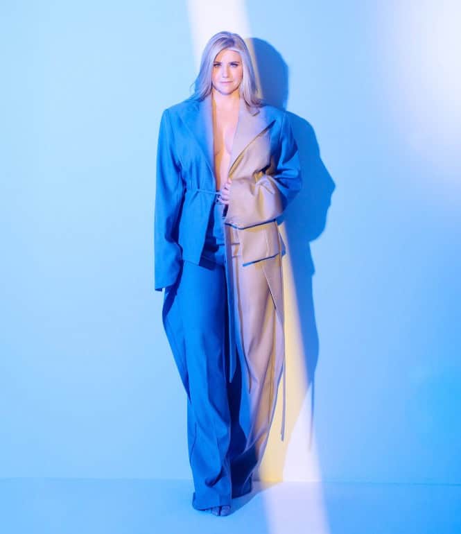 Beatrice Egli in einem blauen, eleganten Anzug mit weitem Schnitt, posierend vor einem hellblauen Hintergrund mit Lichtreflexen.