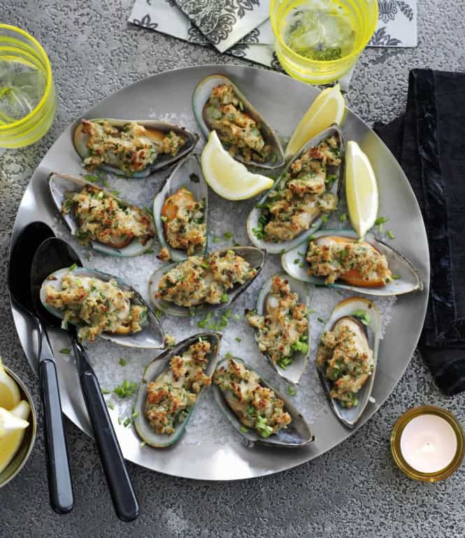 Gegrillte Miesmuscheln mit knuspriger Kräuter-Panade, serviert auf einer Platte mit grobem Salz, Zitronenspalten und Schnittlauch.