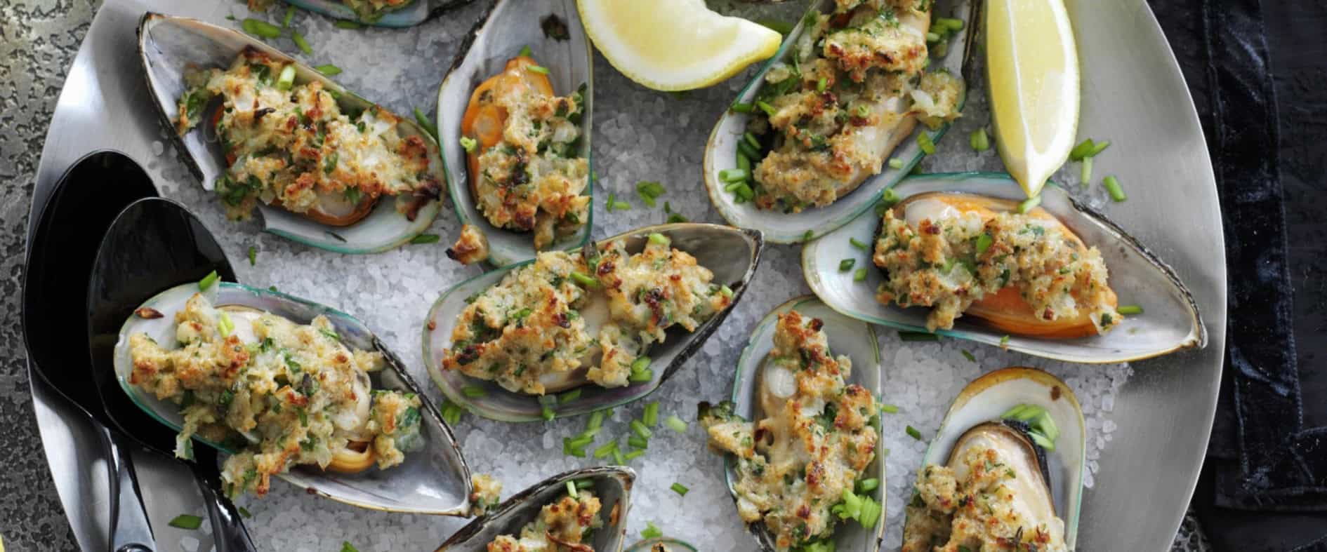 Gegrillte Miesmuscheln mit knuspriger Kräuter-Panade, serviert auf einer Platte mit grobem Salz, Zitronenspalten und Schnittlauch.