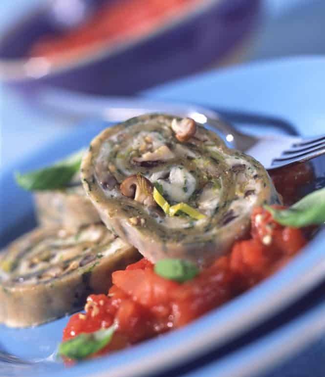 Spinat-Nudelroulade mit Pilzfüllung in Scheiben geschnitten, serviert auf einem Teller mit Tomatensauce und garniert mit frischen Kräutern.