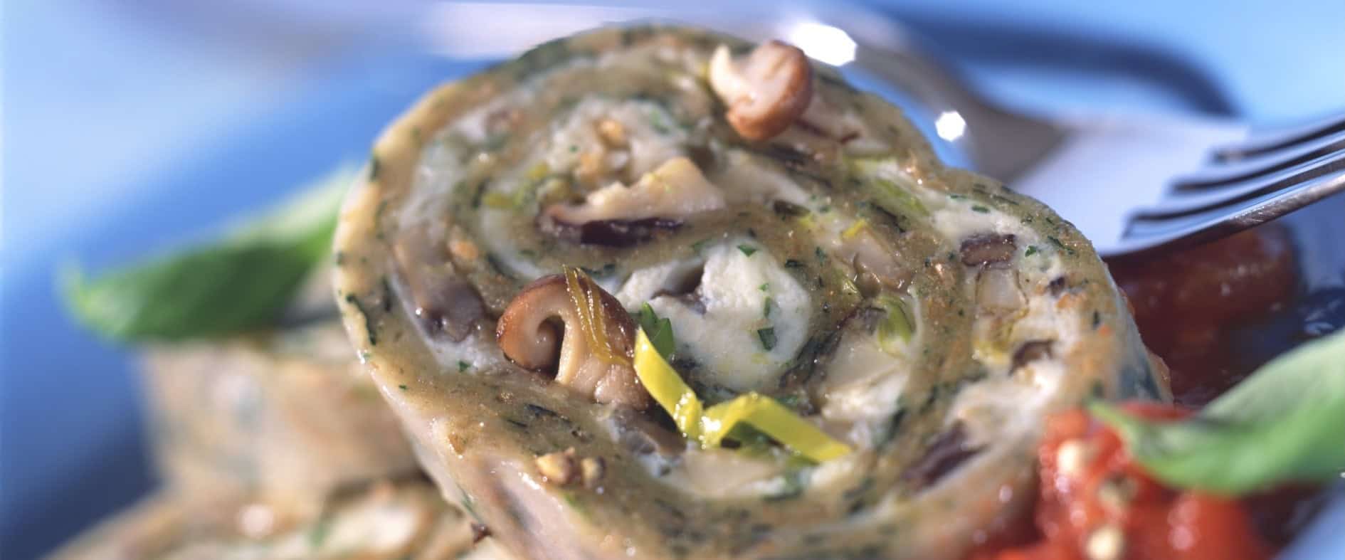 Spinat-Nudelroulade mit Pilzfüllung in Scheiben geschnitten, serviert auf einem Teller mit Tomatensauce und garniert mit frischen Kräutern.