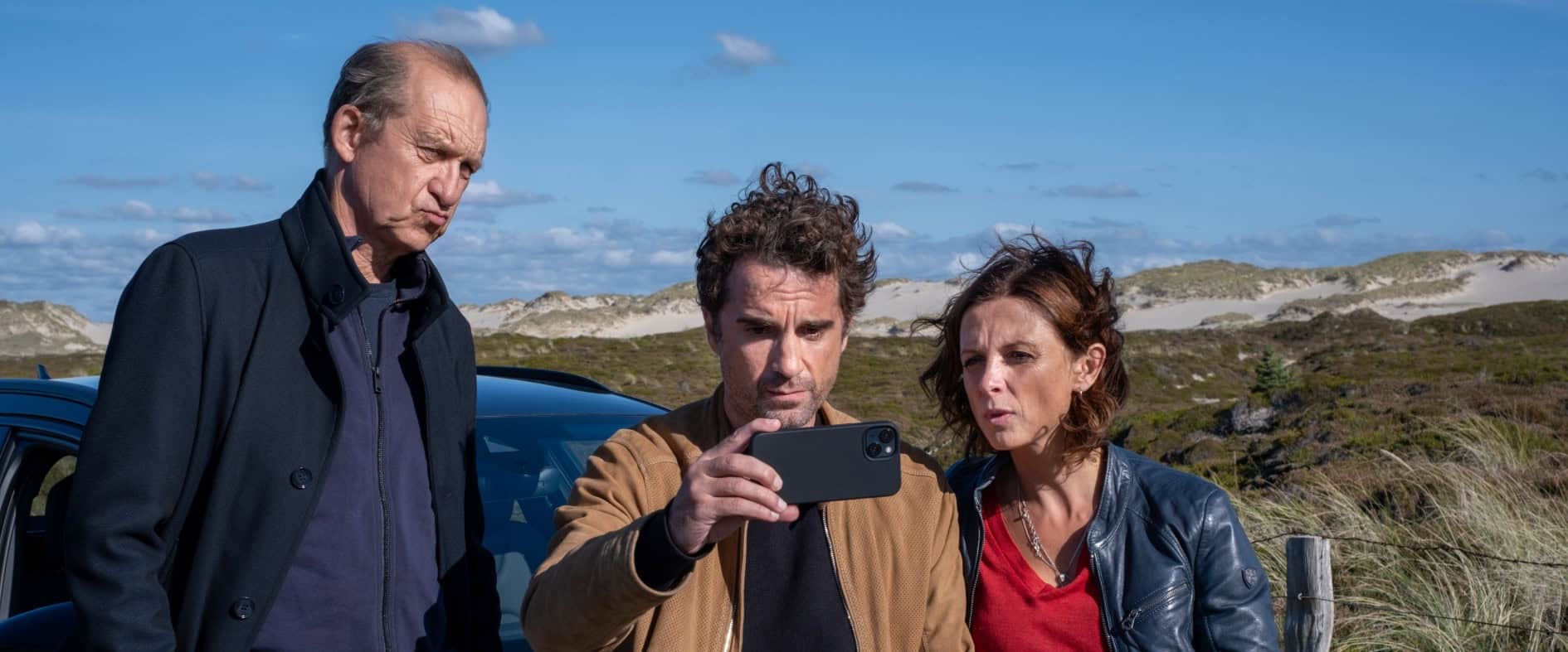Peter Heinrich Brix, Oliver Wnuk und Julia Brendler als Nord Nord Mord-Ermittlerteam vor blauem Auto in Sylter Dünenlandschaft