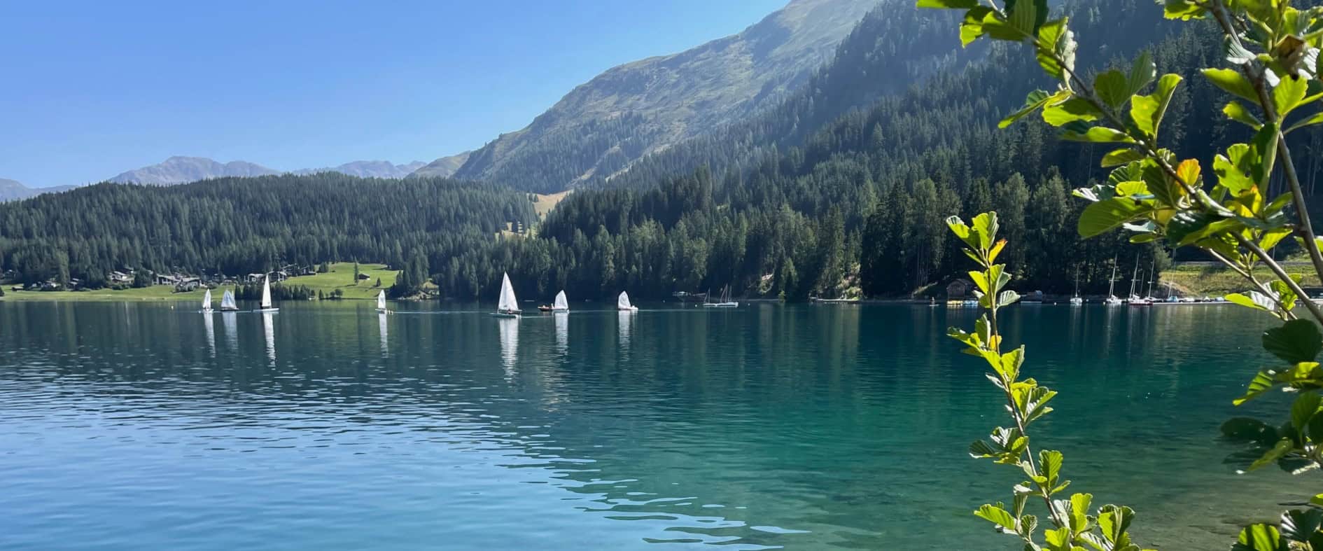 Kristallklarer Davoser See mit Segelbooten und umrahmten Bergen – ein idyllisches Ziel für Naturliebhaber und Wassersportfans in Graubünden.