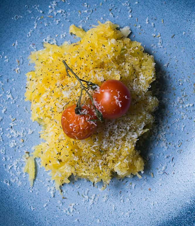 Teller mit Spaghettikürbis als Pasta-Alternative, garniert mit Käse und Tomate, serviert auf Holztisch mit Herbstblättern