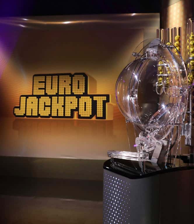 Eurojackpot-Ziehungsstudio. Vorne ist das Ziehungsgerät zu sehen, hinten ein Bildschirm mit dem Eurojackpot-Logo.