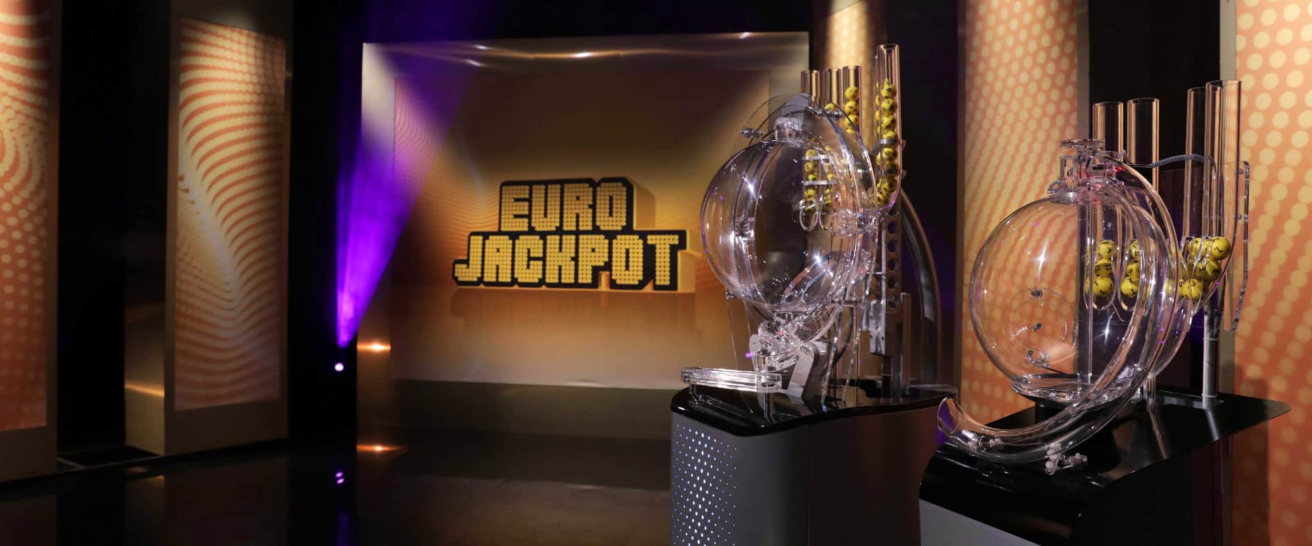 Eurojackpot-Ziehungsstudio. Vorne ist das Ziehungsgerät zu sehen, hinten ein Bildschirm mit dem Eurojackpot-Logo.