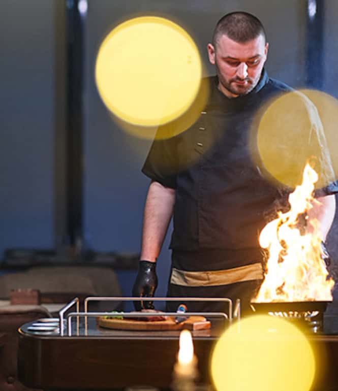 Koch flambiert am Tisch eines Restaurants ein Gericht vor den Gästen