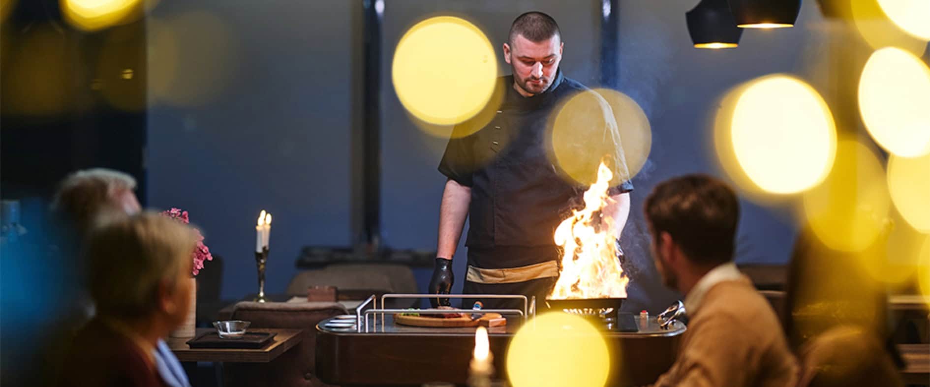Koch flambiert am Tisch eines Restaurants ein Gericht vor den Gästen
