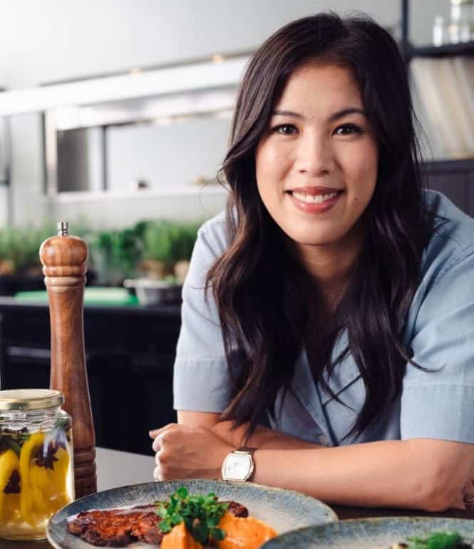 Mai Thi Nguyen-Kim lächelt in einer Küche und stützt sich auf eine Arbeitsplatte, vor ihr mehrere Teller mit Speisen und Gläser mit eingelegten Lebensmitteln